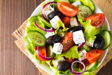 Fresh Greek salad made of cherry tomato, ruccola, arugula, feta, olives, cucumbers, onion and spices. Caesar salad in a white bowl on wooden background. Healthy organic diet food concept.