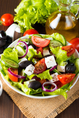 Fresh Greek salad made of cherry tomato, ruccola, arugula, feta, olives, cucumbers, onion and spices. Caesar salad in a white bowl on wooden background. Healthy organic diet food concept.