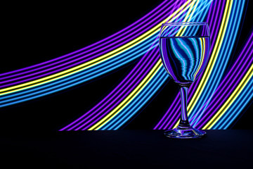 Wine glass isolated against a black background with colorful streaks of neon light painting behind them