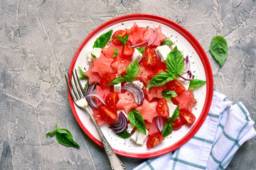 Watermelon salad with tomato, feta cheese, red onion and basil on a plate.Top view with copy space.