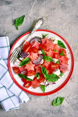 Watermelon salad with tomato, feta cheese, red onion and basil on a plate.Top view with copy space.