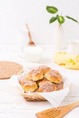 Cottage cheese cookies sprinkled with sugar in a basket and a cup of milk on a wooden table