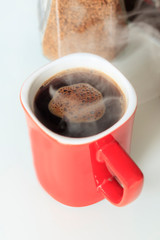 red mug. coffee is poured into it. He is a true steam. next to the glass jar, coffee granules are opened in it