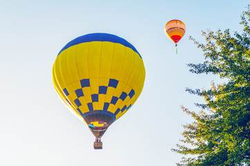 Colorful hot air balloon is flying in the blue sky above the trees