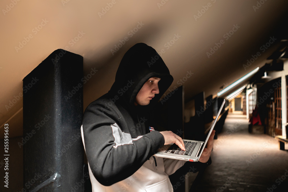 Wall mural portrait of young geek in hood in dark room with laptop