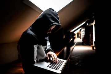portrait of young geek in hood in dark room with laptop