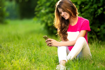Beautiful woman using tablet sitting on grass in the green park.