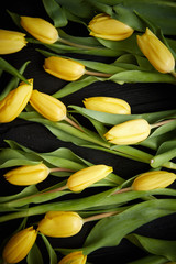 Obraz premium Yellow tulips placed on black table. Top view with flat lay