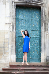 Fototapeta na wymiar Young girl posing in a blue dress for the camera on a background of green metal door. Confident stylish woman looks to the side