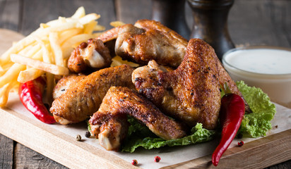 Close-up photo of bbq chicken wings with fries and beer. Barbeques meat with sauces, ketchup, mayonnaise. Fast and junk food concept. 