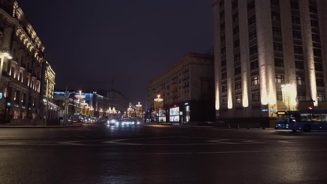 The bendy bus passes the intersection at night. In the background, the night city, the houses are beautifully illuminated with majestic architecture.