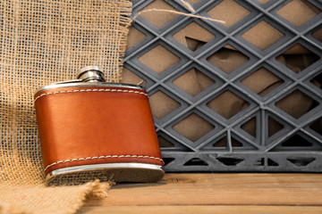 A leather covered stainless steel flask against a milkcrate and burlap.