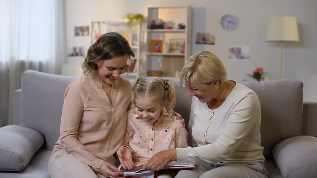 Granny and mother showing photo album pictures to small girl, family history