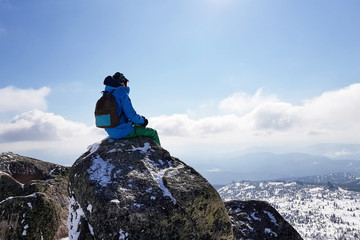 Traveler with a backpack sits on top of a mountain