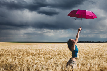Young woman with umbrella on wheat field in storm time