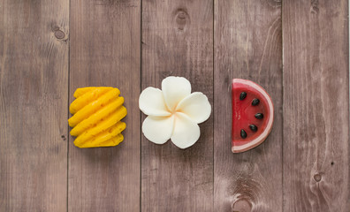 Hand made soap in the shape of fruit yellow pineapple, watermelon and flower on wooden background.