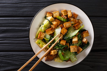 Stir fry tofu with bok choy and sesame seeds close-up on a plate. horizontal top view