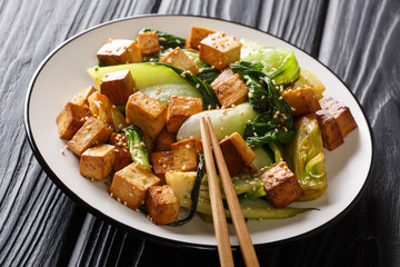 Veggie fried tofu with baby bok choy, soy sauce and sesame seeds closeup on the table. horizontal