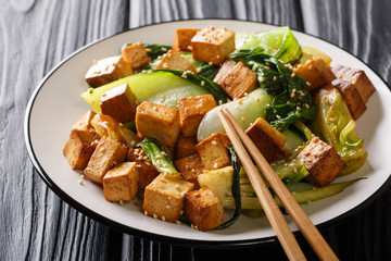 Traditional fried tofu with bok choy, soy sauce and sesame close-up on a plate. horizontal