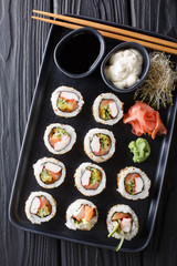 Uramaki rolls set served with sauces, soy sprouts, ginger and wasabi closeup on a plate. Vertical top view