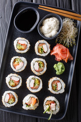 set of Japanese rolls uramaki served with sauces, ginger and wasabi closeup on the table. Vertical top view