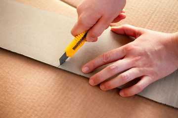 Snap-off knife in person hands cutting cardboard.