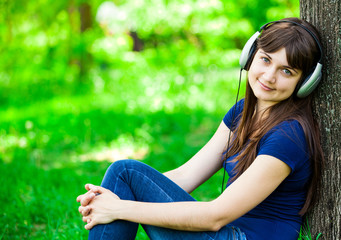Naklejka na ściany i meble Young fashion girl with headphones at green spring grass.