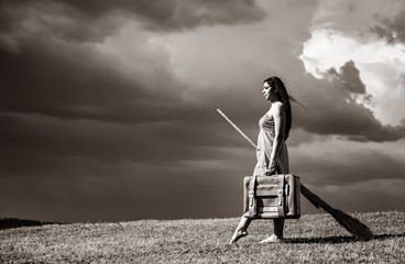Young witch at grass field with broom in storm day.