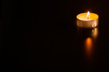 One burning candle in the corner on black, space for text