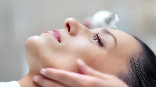 Close-up face of confident pretty woman during microdermabrasion beauty procedure using equipment
