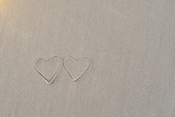 Two heart shapes written in the sand on the beach morning sunlight.