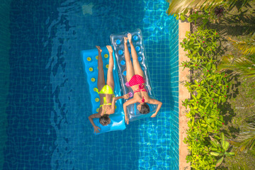 aerial top view above swimming pool. woman in yellow bikini and woman in red bikini sleep on swimming pool inflatable .mattress float in villa pool