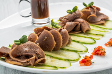 Boiled beef tongue on dark wooden table with pesto and salad