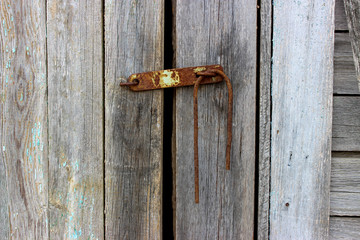 Old padlock. With a metal rod. The metal is old, rusty with traces of peeling blue paint.  Wooden door, gray, cracked. The texture of the Board. Rural yard. Background, texture.