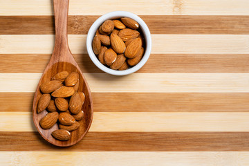 Natural almond in wooden spoon and pot on bamboo striped table.