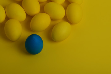 One blue painted Easter egg stands in front of yellow eggs on a yellow background. Happy Easter holiday card or banner. Copy space.