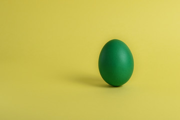 One green painted Easter egg stand on a yellow background. Happy Easter holiday card or banner. Copy space.