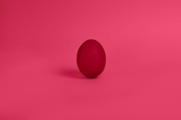 One red painted Easter egg stand on a pink background. Happy Easter holiday card or banner.