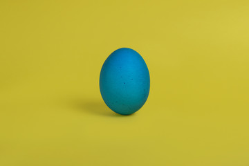 One blue painted Easter egg stand on a yellow background. Happy Easter holiday card or banner. 