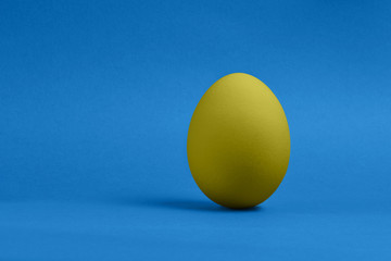 One yellow painted Easter egg on blue background. Happy Easter holiday card or banner. Copy space.