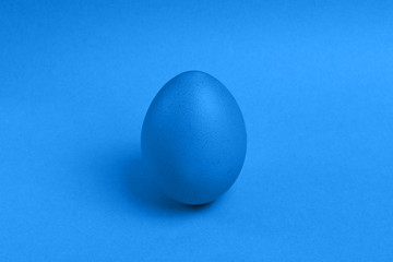 One blue painted Easter egg stand on a blue background. Happy Easter holiday card or banner.