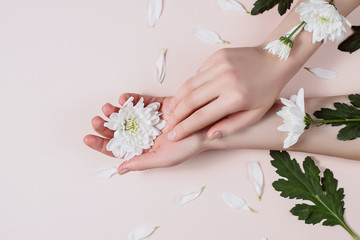 Young perfect female hands with white flowers on pastel pink background. Care about nails and clean, soft, smooth skin. Manicure, pedicure beauty salon. Flat lay, top view, copy space.