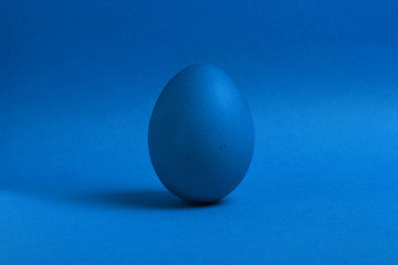 One blue painted Easter egg stand on a blue background. Happy Easter holiday card or banner. Copy space