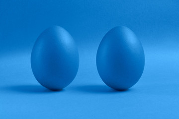 Two blue painted Easter eggs stand on a blue background. Happy Easter holiday card or banner.