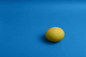 One yellow painted Easter egg on blue background. Happy Easter holiday card or banner. Copy space.