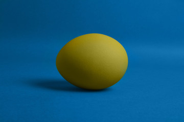 One yellow painted Easter egg on blue background. Happy Easter holiday card or banner. 