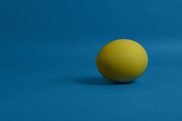 One yellow painted Easter egg on blue background. Happy Easter holiday card or banner. Copy space.