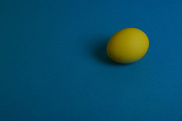 One yellow painted Easter egg on blue background. Happy Easter holiday card or banner. Copy space.