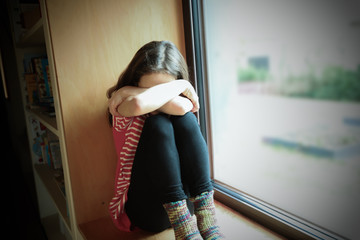 Ein Mädchen sitzt ängstlich auf der Fensterbank 