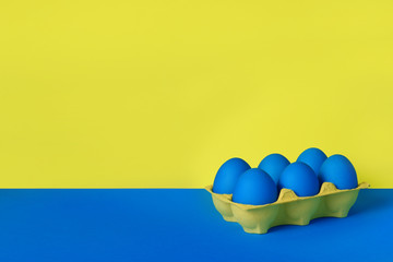 Six blue painted Easter eggs in yellow wrapping on blue and yellow background. Happy Easter holiday card or banner. Copy space.